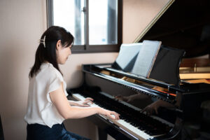 グランドピアノで楽譜を見ながら演奏するピアノ講師の様子