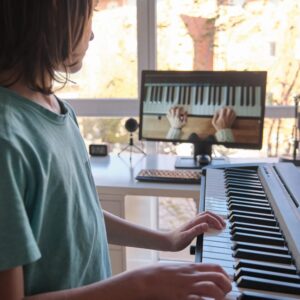自宅で電子ピアノを弾く子どもが、画面に映る鍵盤の映像を見ながらオンラインレッスンに取り組んでいる様子。